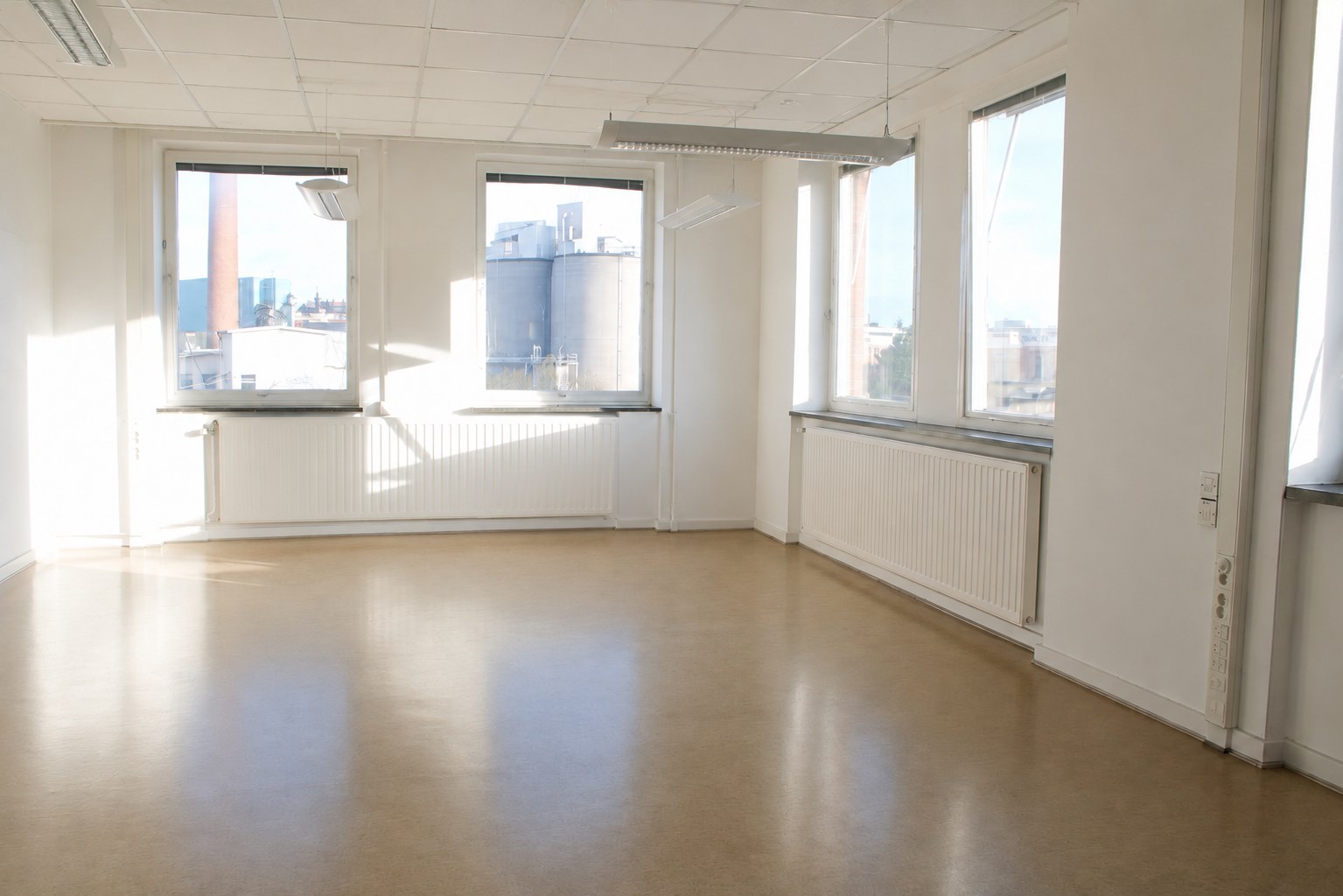 An empty studio at Färgkontoret in afternoon sun, with a cork floor and windows on two walls