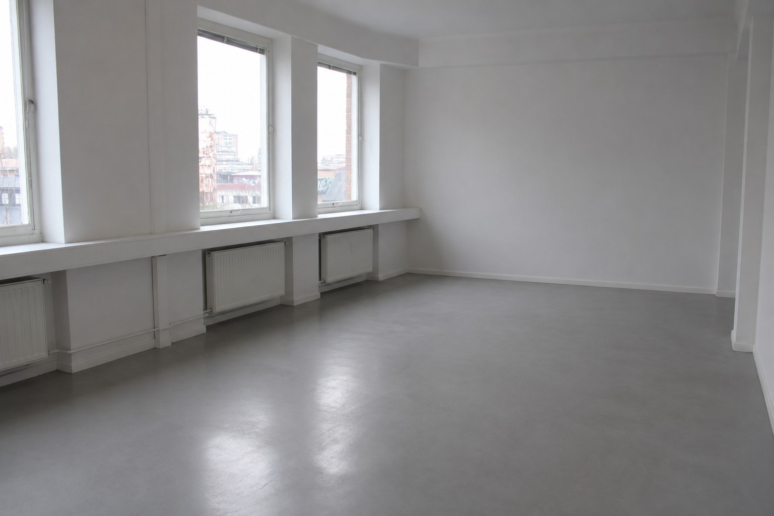 An empty studio at Färgkontoret with a grey resin floor and a row of windows along one wall